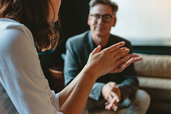 A woman talking to a man whose wearing a suit attire and glasses.